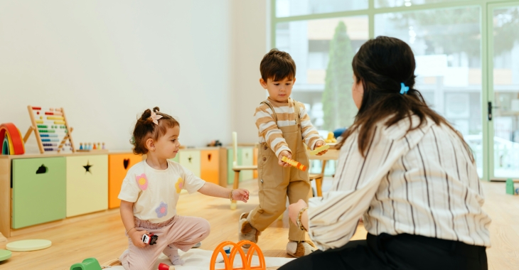 Kinderbegeleider speelt met peuters op speelmat