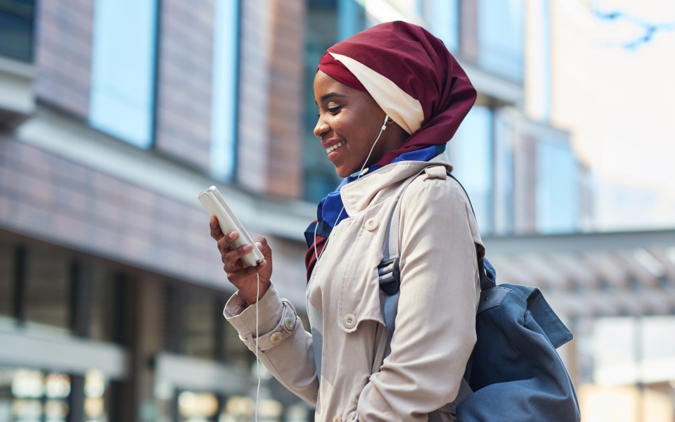 Vrouw met hoofddoek kijkt al lachend naar smartphone en luistert naar muziek via oortjes