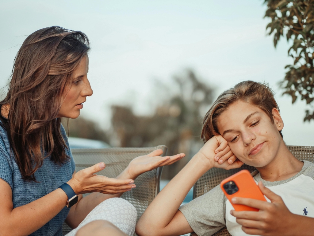Volwassene praat met tiener die naar een smartphone kijkt.