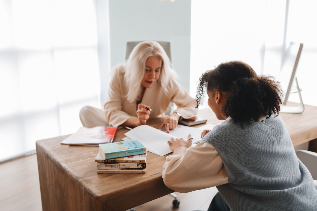 Begeleider bespreekt schoolwerk met een leerling aan een bureau met boeken.