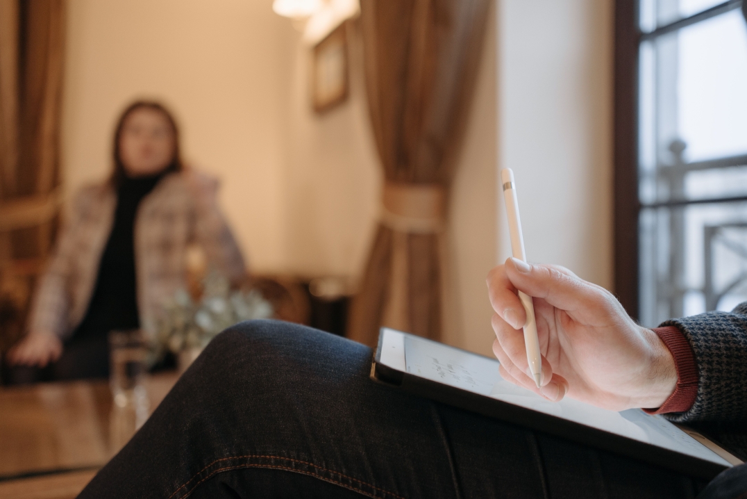 Begeleider maakt notities tijdens een gesprek met een cliënt in een rustige ruimte.