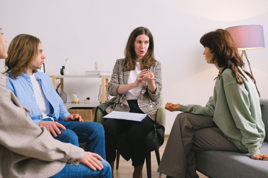 Groep mensen neemt deel aan een begeleid gesprek in een rustige gespreksruimte.