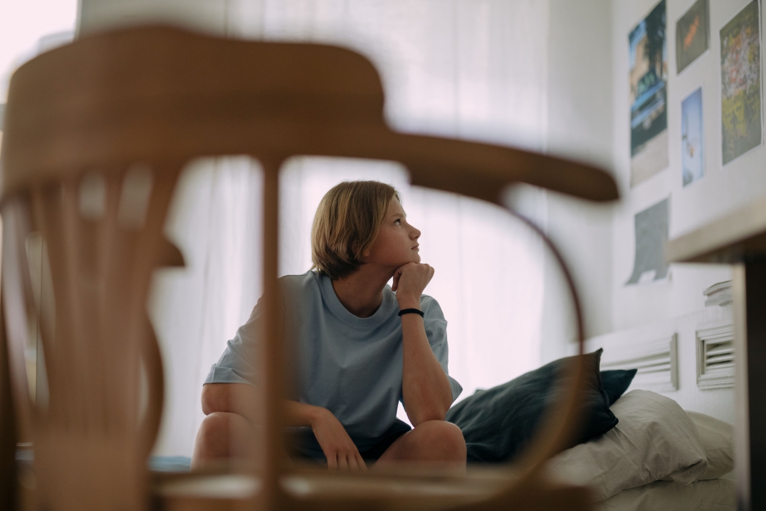 Een jongere zit op een bed en kijkt nadenkend naar foto's en afbeeldingen aan de muur.