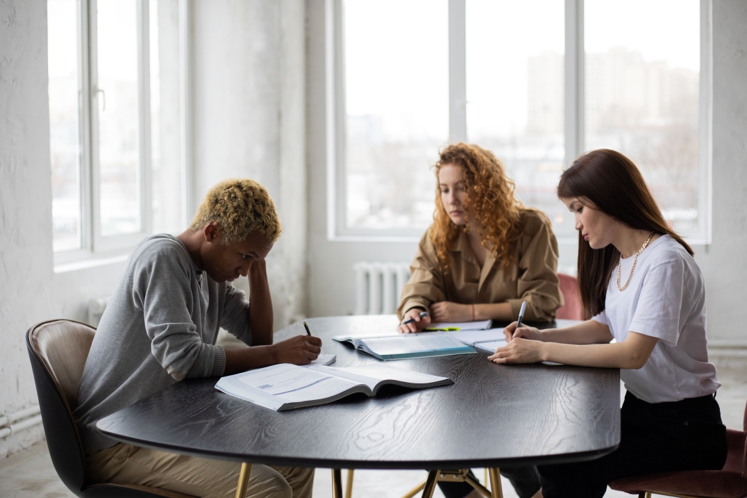 Drie jongeren werken samen aan school- of studietaken aan een tafel met boeken en notities.
