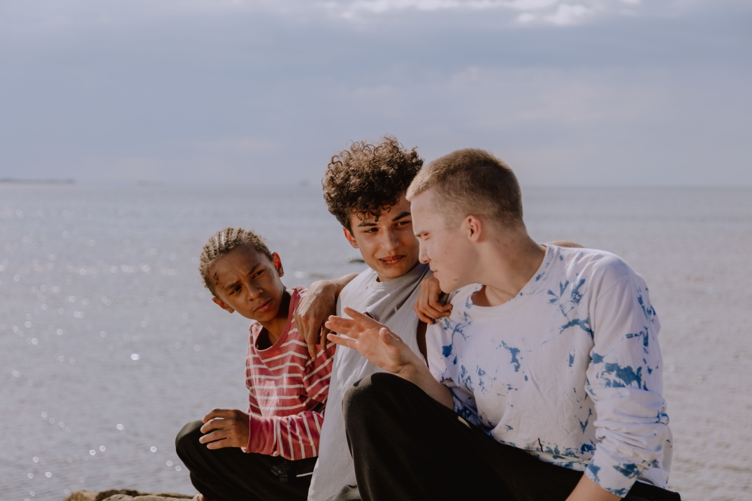 Drie jongeren zitten samen aan het water en praten ontspannen met elkaar.