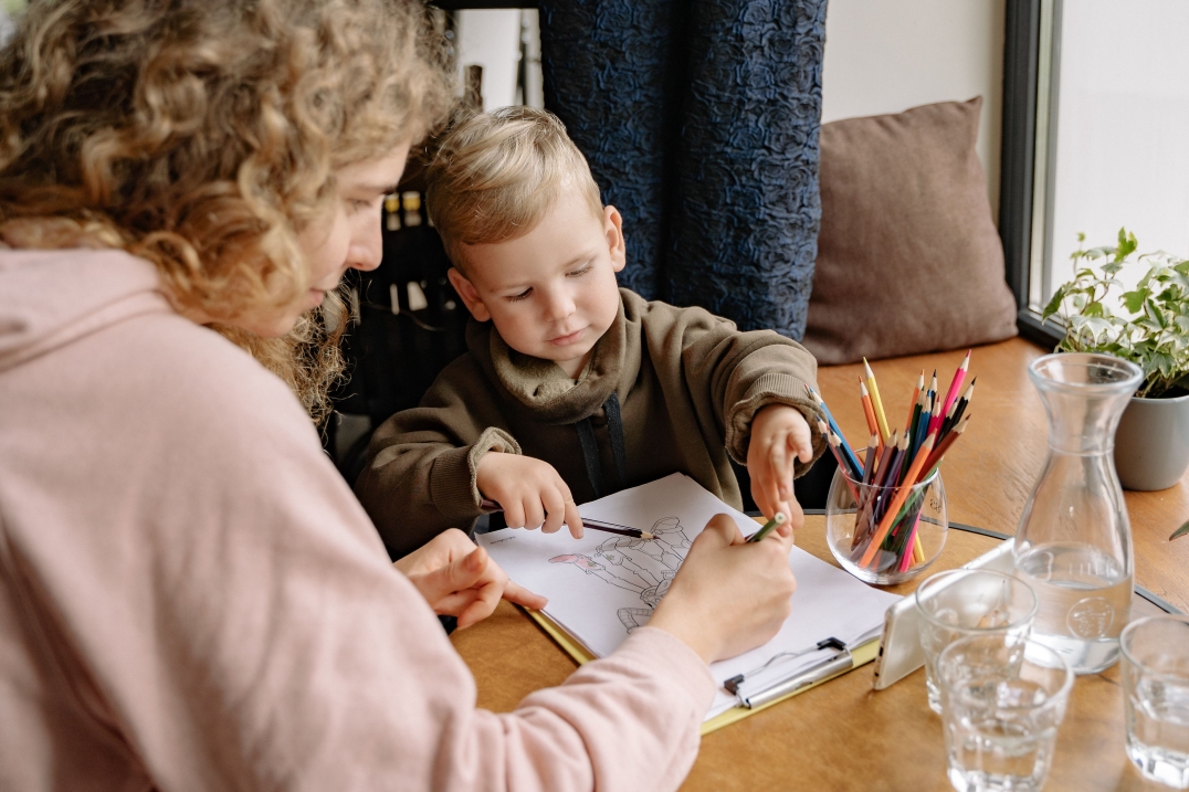 Ouder en kind kleuren samen een tekening aan tafel met kleurpotloden.
