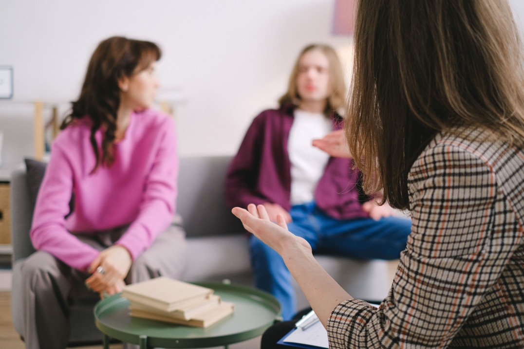 Drie vrouwen voeren een gesprek in een praktijkruimte.