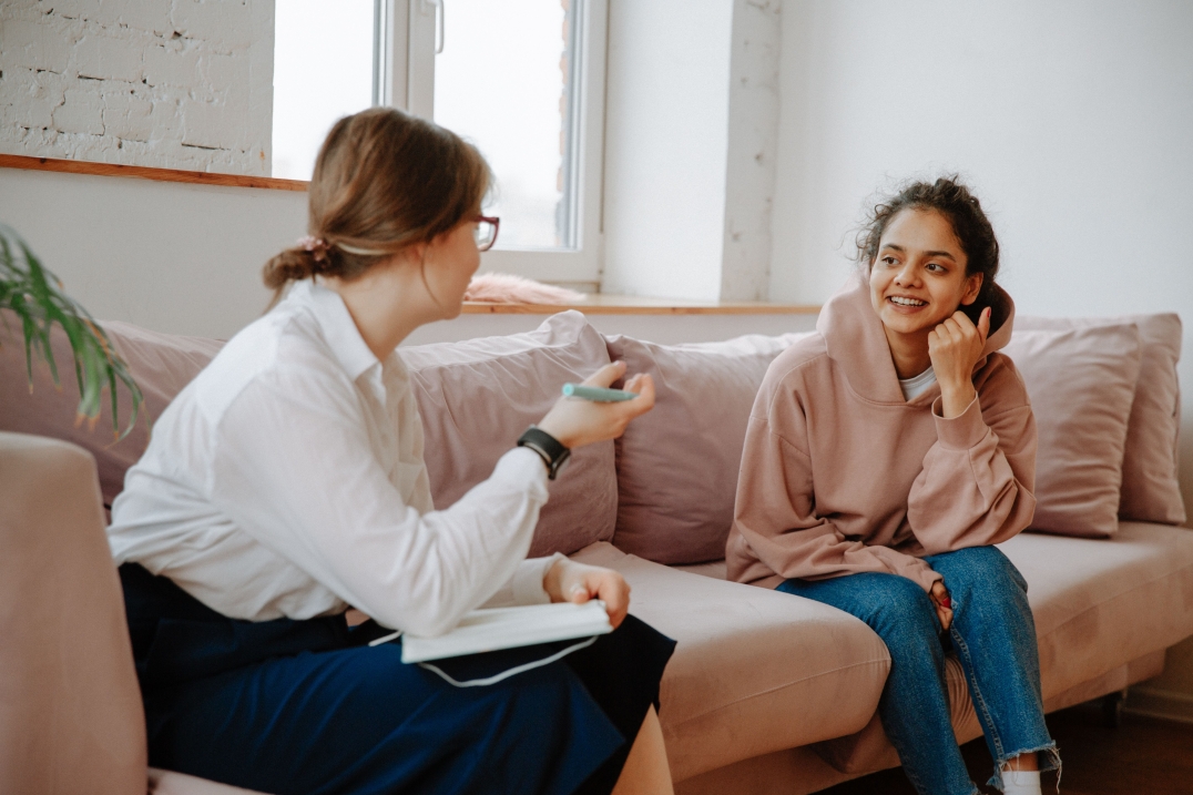 Twee vrouwen voeren een gesprek op een bank in een lichte en rustige ruimte.