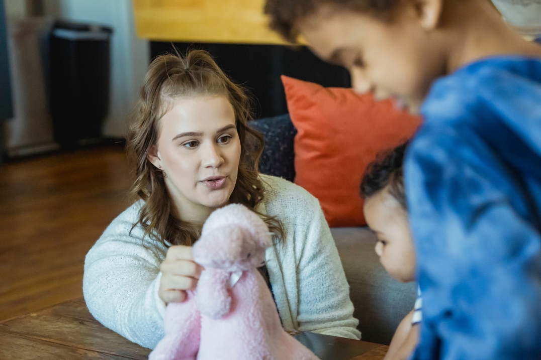 Vrouw speelt met twee jonge kinderen aan tafel.