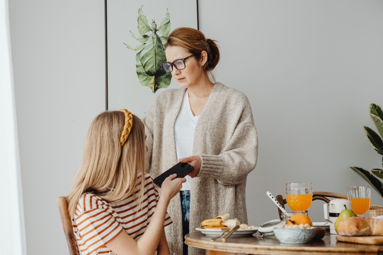 Volwassene geeft een smartphone aan een kind aan de ontbijttafel.